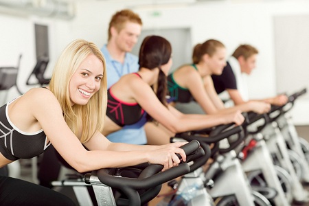 Young fitness people doing spinning with instructor at gym