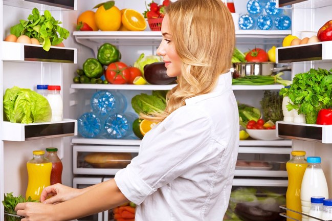 Uma mulher observando os grupos de alimentos na geladeira que ajudam a saúde bucal
