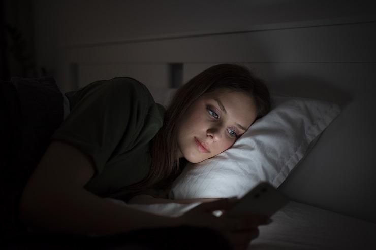 Uma mulher jovem usando o celular na cama, ou seja, precisando de um detox digital antes de dormir.